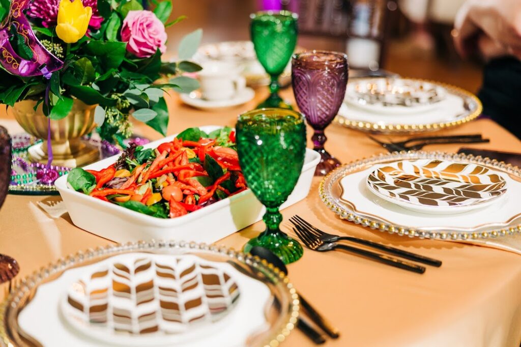 The image is of a table set with plates of food, including a birthday cake, dessert, baked goods, and wine glasses. It showcases a variety of dishes and serveware for a dining or banquet setting